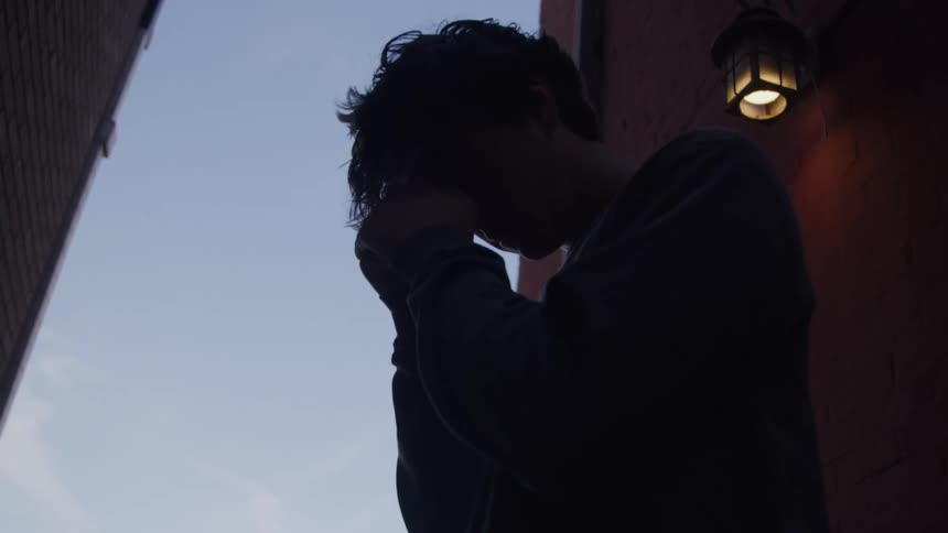 Man with his hands on his head expressing distress in a dim alley