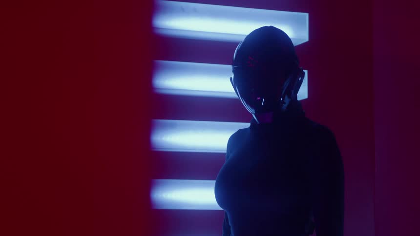 A person in a futuristic helmet turns their head in a room with red and blue neon lights
