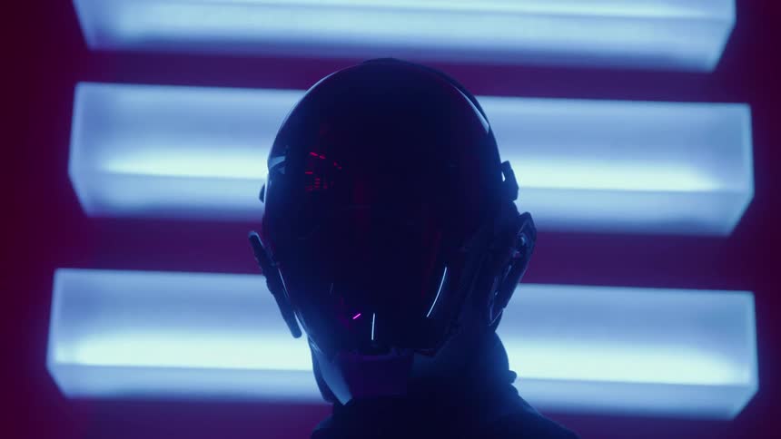 Silhouetted against horizontal blue lights a person in a futuristic helmet slowly turns their head