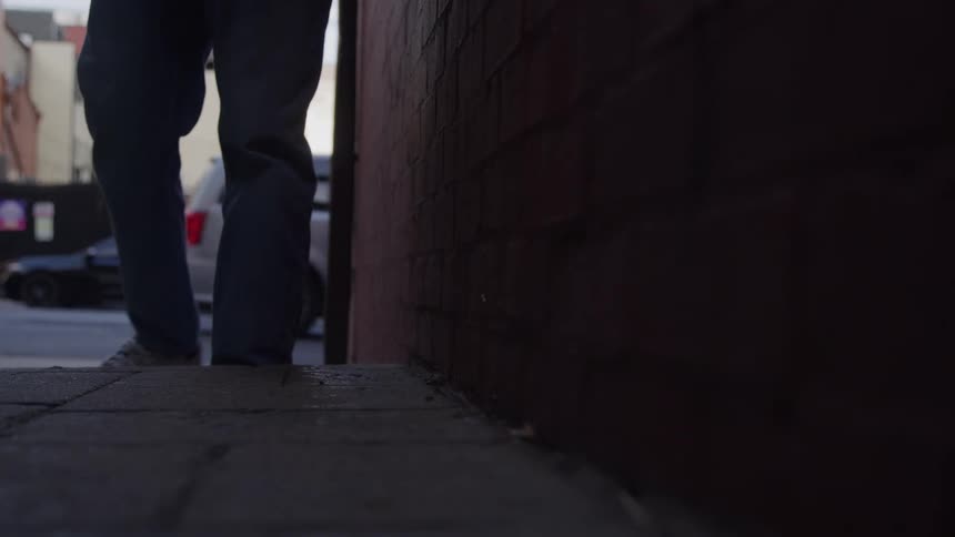 Man walks next to a building and picks up a book from the sidewalk