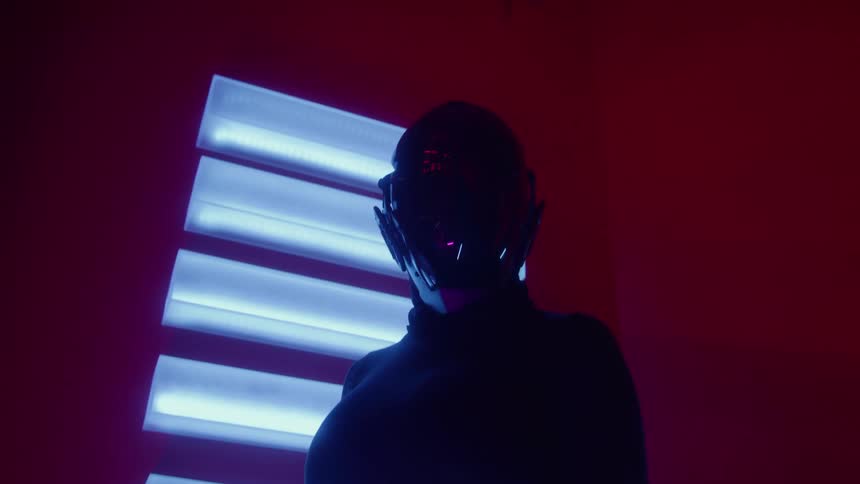 Figure wearing a futuristic helmet illuminated by neon lights in a red setting