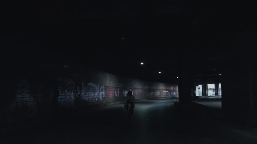 Cyclist rides through a dark tunnel with dim lights illuminating the path