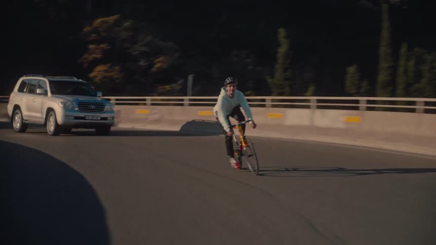 A man riding a bicycle on an overpass road causing a car line to build up behind him