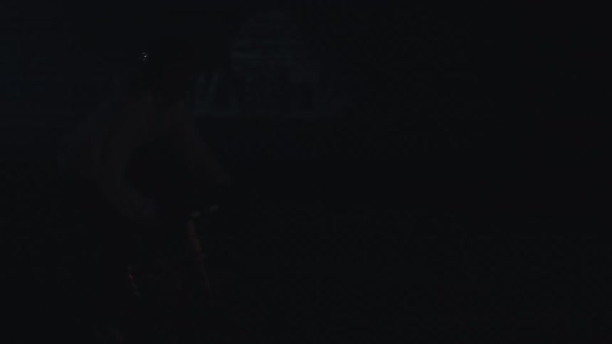 A person wearing a hoodie and helmet rides a bicycle through a dimly lit tunnel with graffiti on the wall