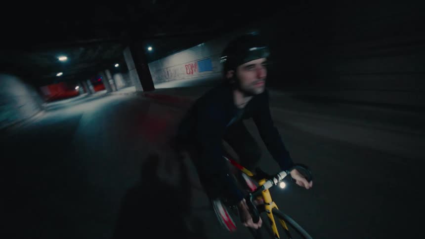 A young man cycling through a road tunnel in a metropolitan city at night