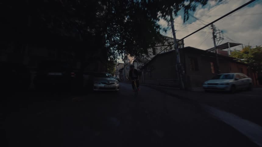 Cars parked on a street as a man rides his bicycle fast through the neighborhood as a child watches