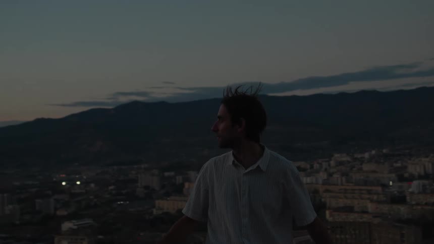 A man standing on a lookout point over a large city taking off a bicycle helmet