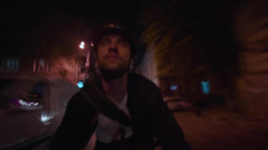 A man rides his bike swiftly through a dimly lit urban street at night