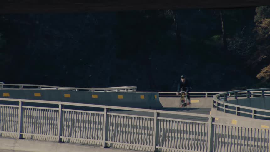 A person on a bicycle rides along a curved elevated roadway ramp followed by a dark suv