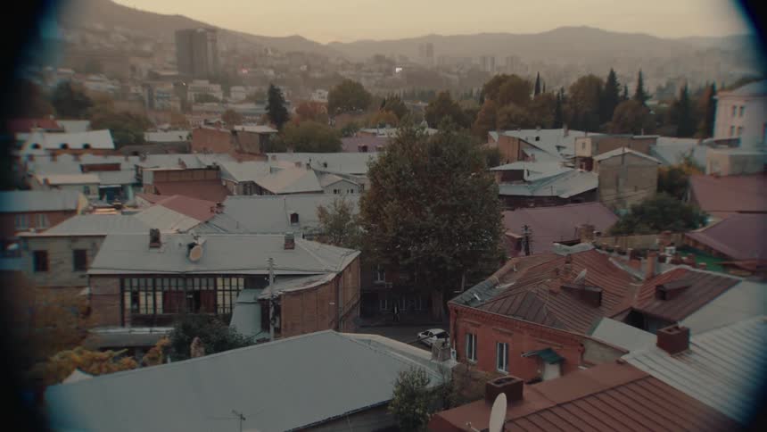 A man standing on a street holding a bicycle under a tree seen from a telescope that zooms out to show the entire cityscape