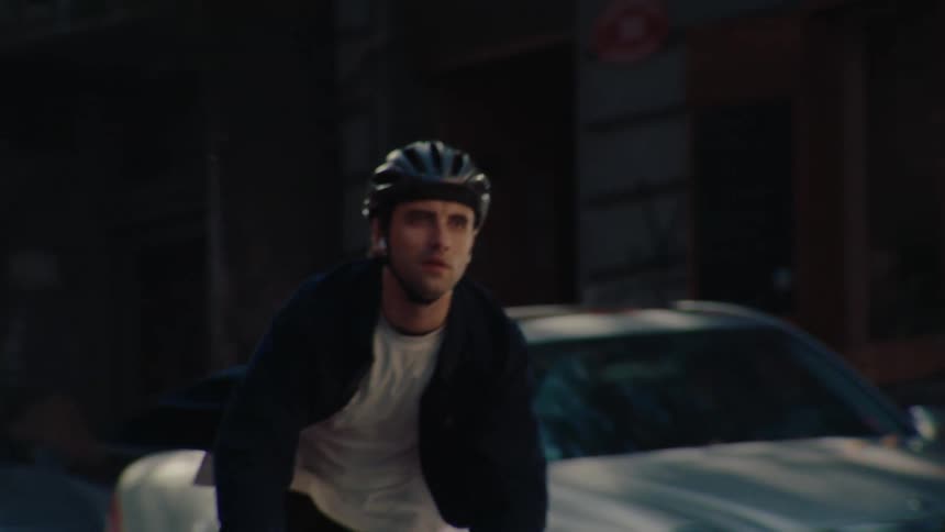 Male cyclist pedals his bicycle between the parked cars lining a street