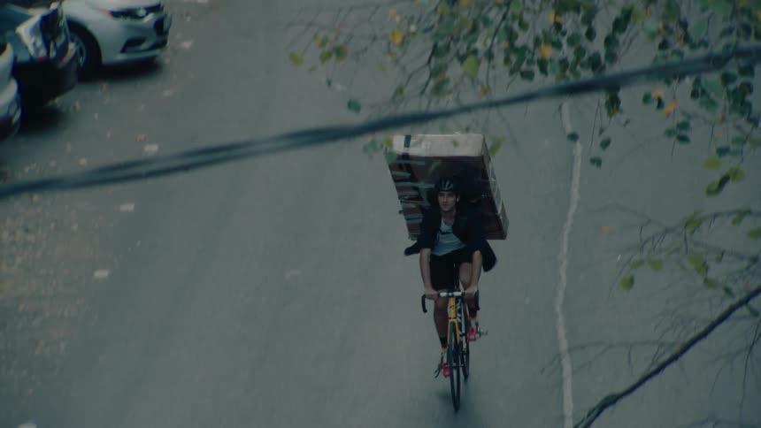 Cyclist carries a large box on his back while riding through an urban street