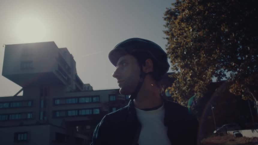 A man with a helmet on is standing near a tree with leaves changing color in the city