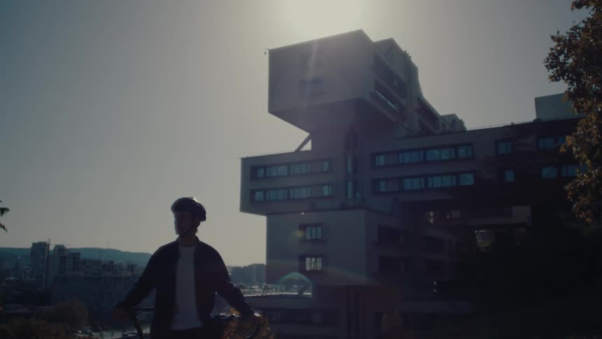 Cyclist looks at the city beside a modern building under sunlight