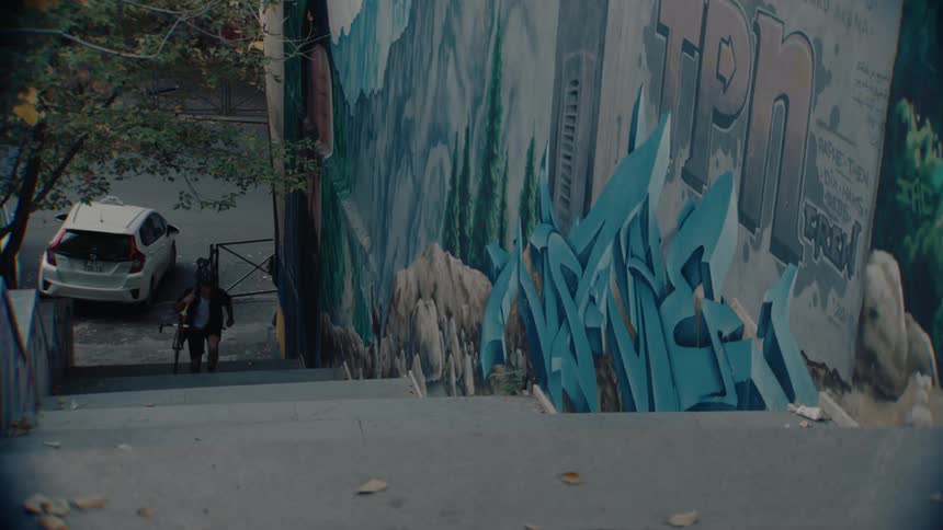 A man carrying a bicycle on his shoulder is climbing the concrete staircase beside a wall covered in graffiti