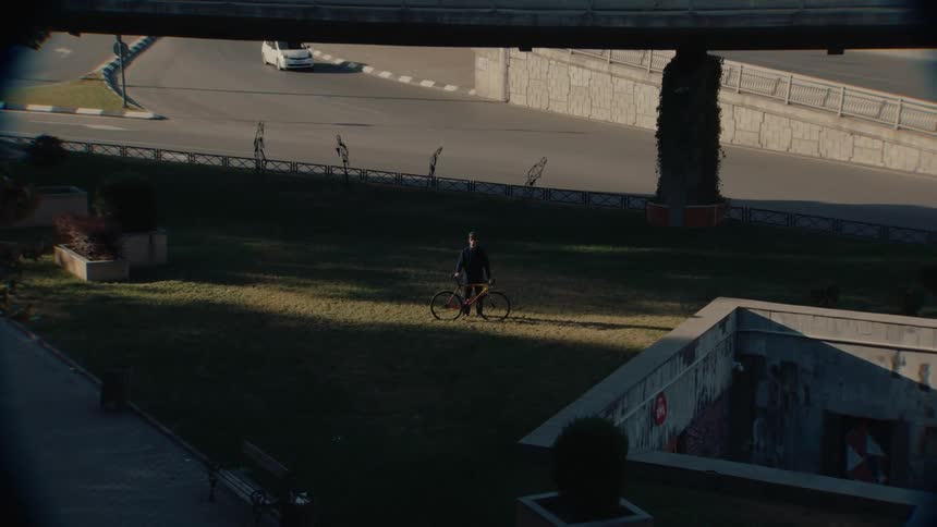 Cyclist standing on a grassy area under a beam of sunlight