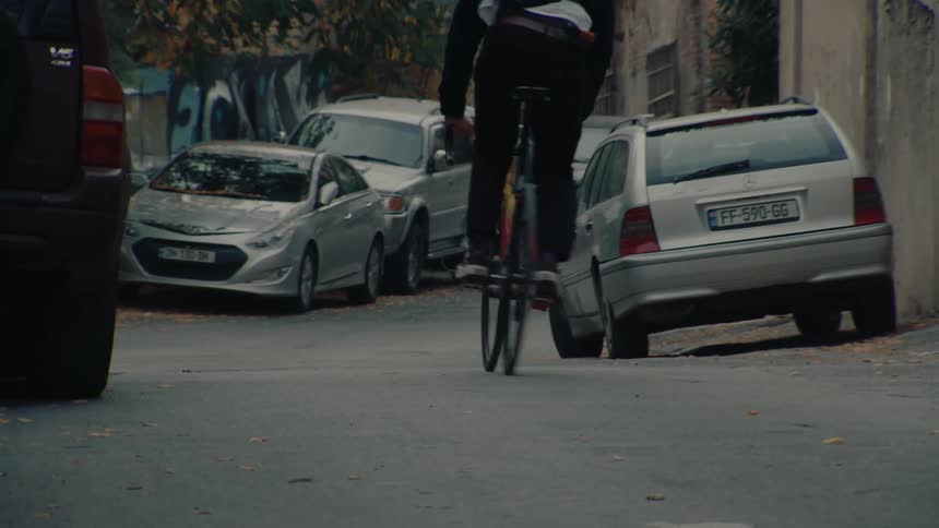 Cyclist rides through a narrow street lined with parked cars