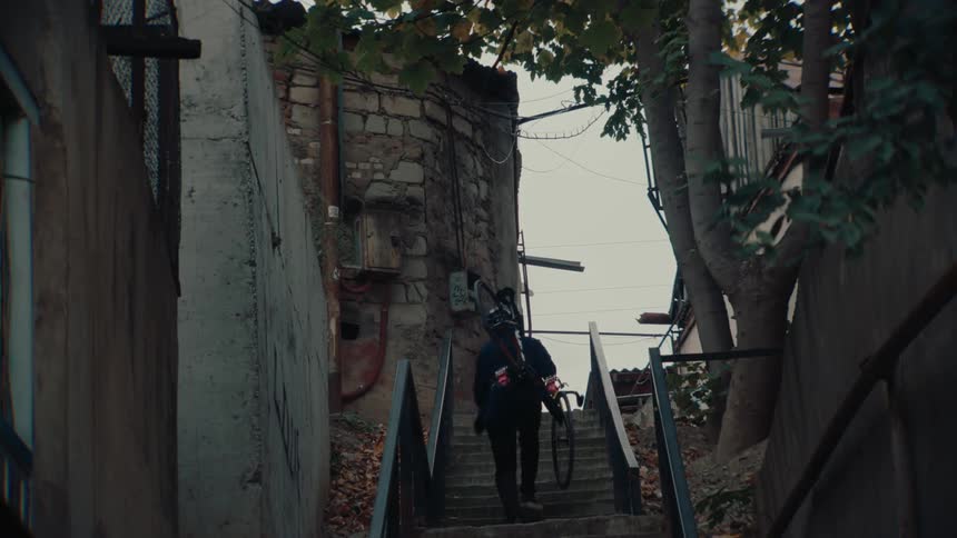 Cyclist climbs a staircase carrying a bicycle in an old urban area