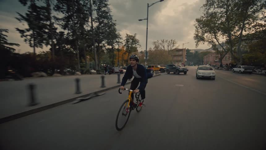 Cyclist rides along a treelined street under a cloudy evening sky