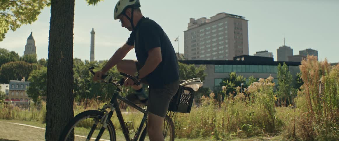 Man leans his bicycle against a tree trunk and takes a beekeeping smoker out of the basket