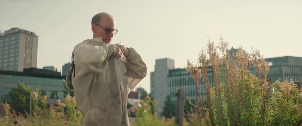 Man standing in a field outside of town putting on a beekeeping suit