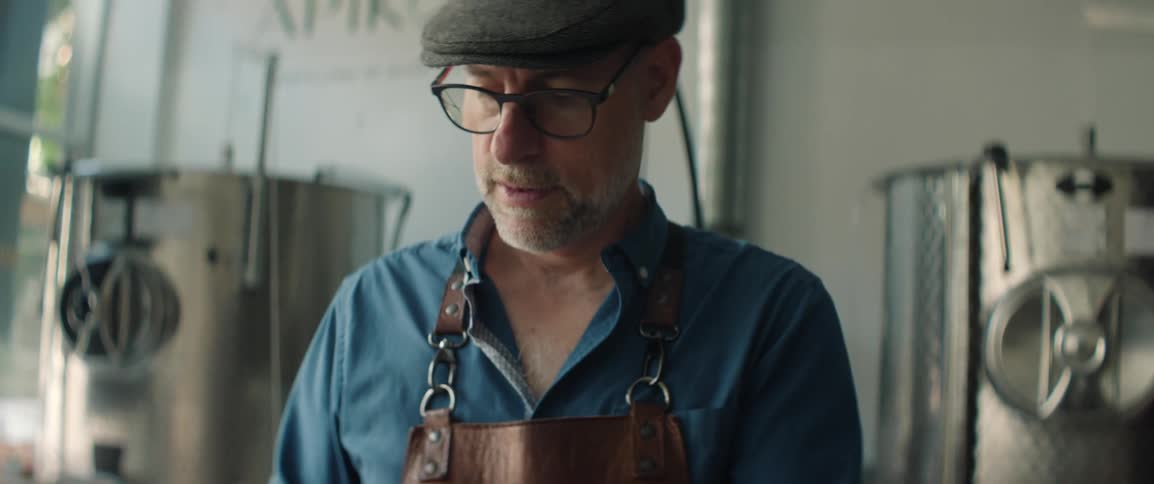 Man wearing a leather apron uses a cellphone in an industrial setting