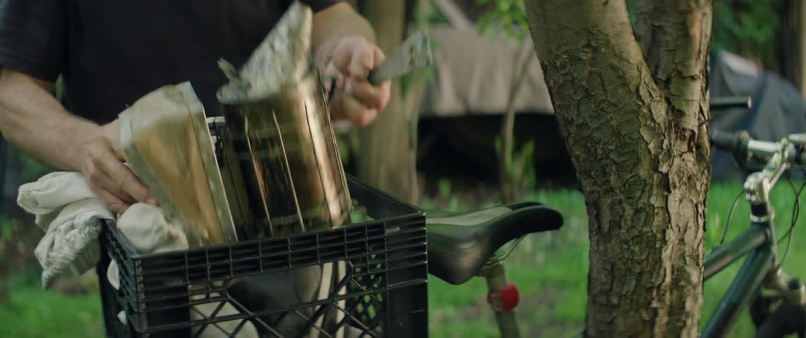 A man walks to a bike and puts beekeeping tools into a basket and wheels away