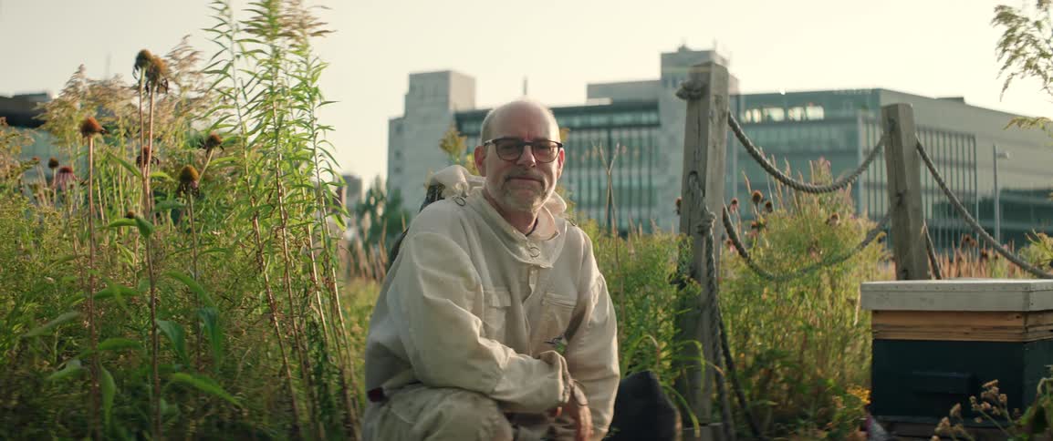 Beekeeper in protective clothing kneels near beehives in an urban field