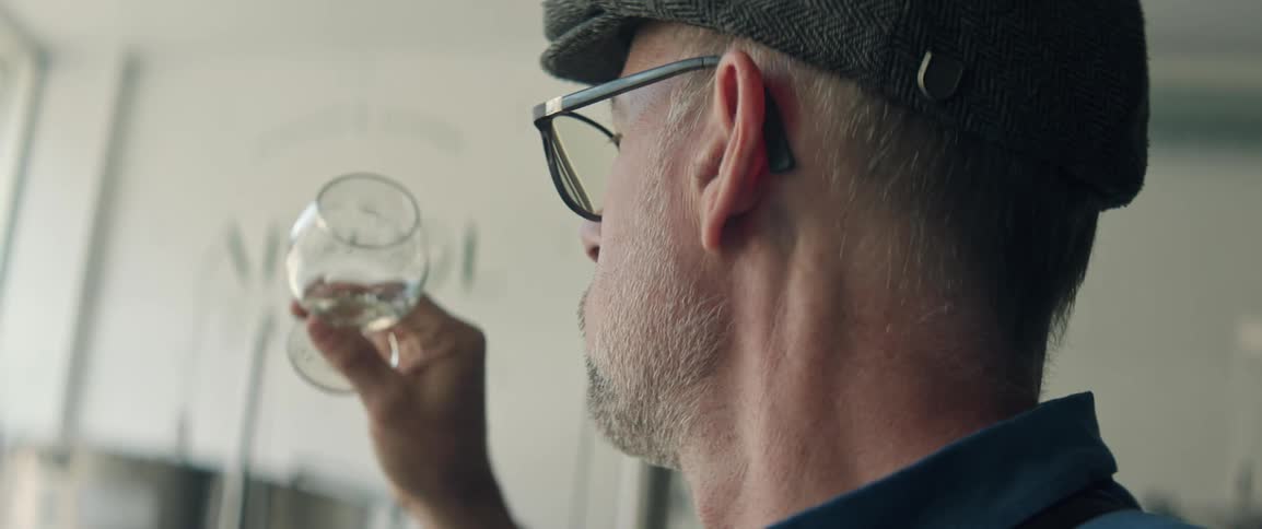 Man working in a distillery examines the liquor in a glass during the daytime
