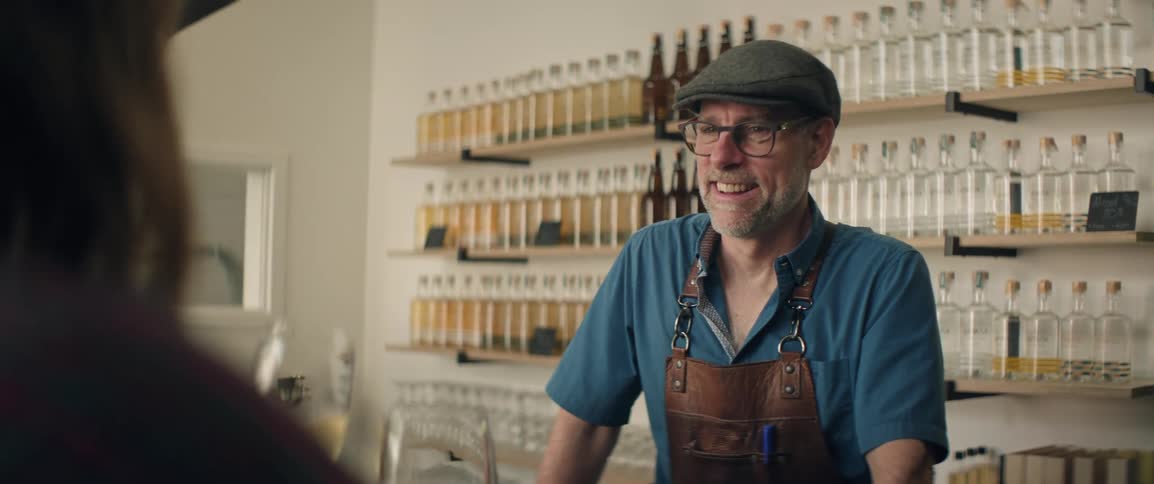 Man smiles behind the counter as a customer raises a glass of drink