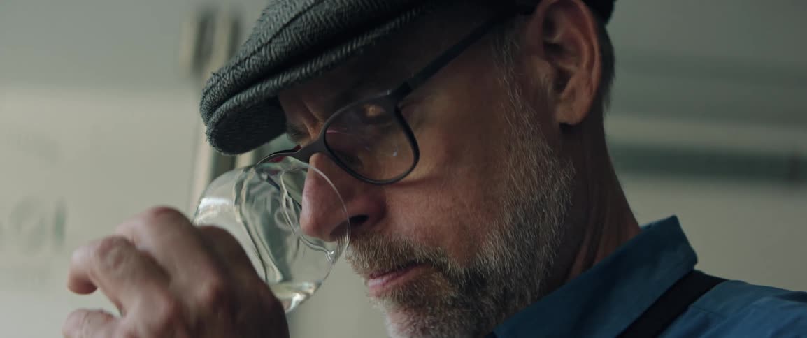 A man holds a small glass of liquor up to his nose to smell it
