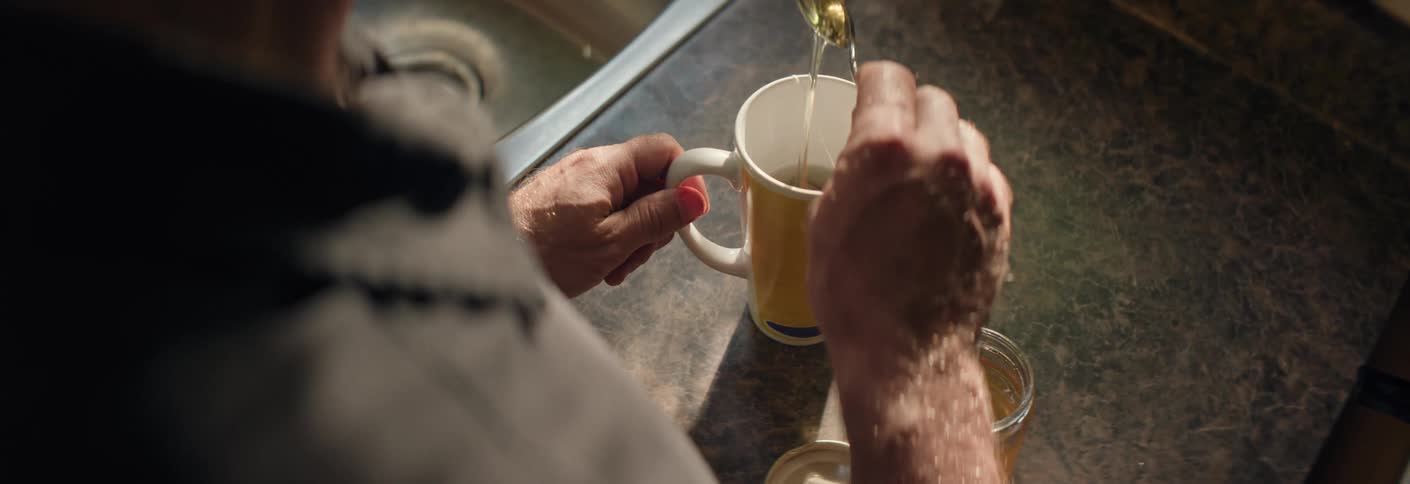 Man adds honey into a mug on a sunlit counter