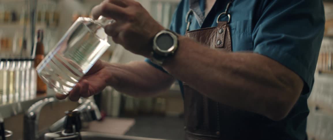 A bartender selects a bottle of liquor from a shelf and shows it to a customer