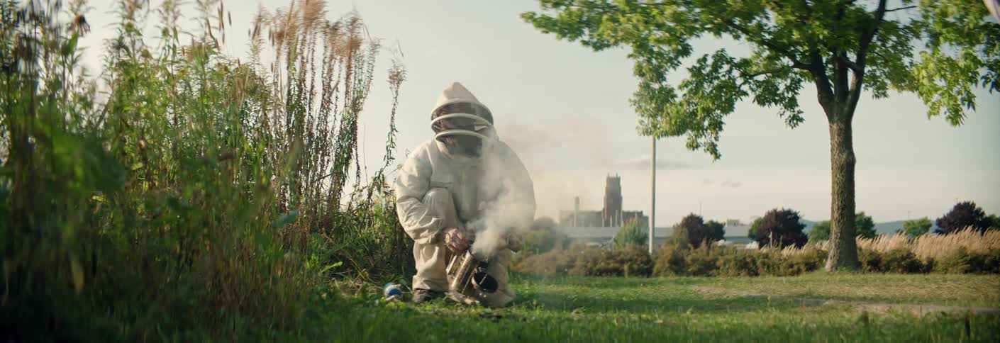 Beekeeper crouches on the grass using a smoker near beehives