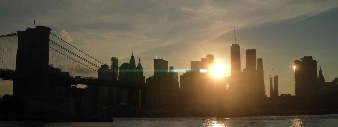 Sun sets behind skyscrapers near the bridge over the river