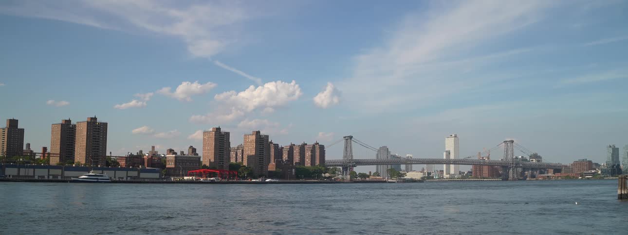 Urban view shows buildings and a bridge over the river under a blue sky with clouds