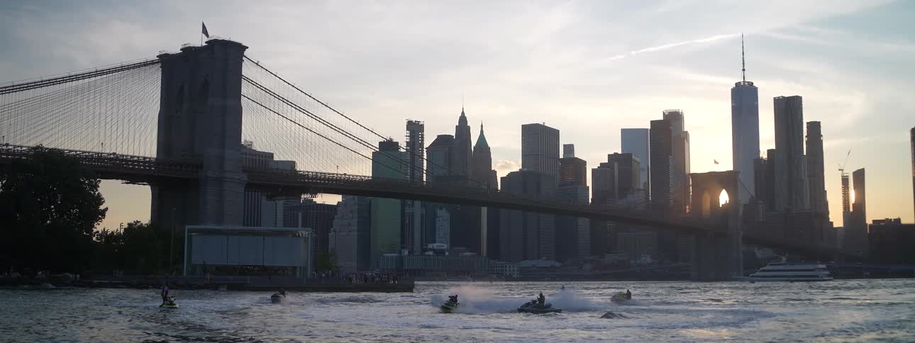 Brooklyn bridge with towers and skyscrapers on the manhattan skyline as boats sail on the east river