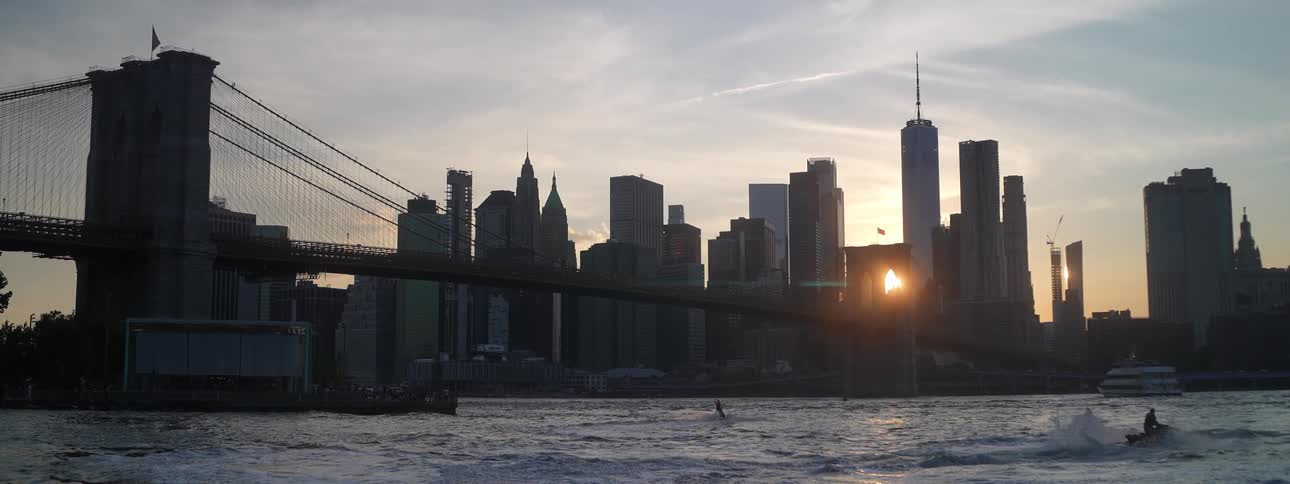 Brooklyn bridge with towers and skyscrapers on the manhattan skyline as boats sail on the east river