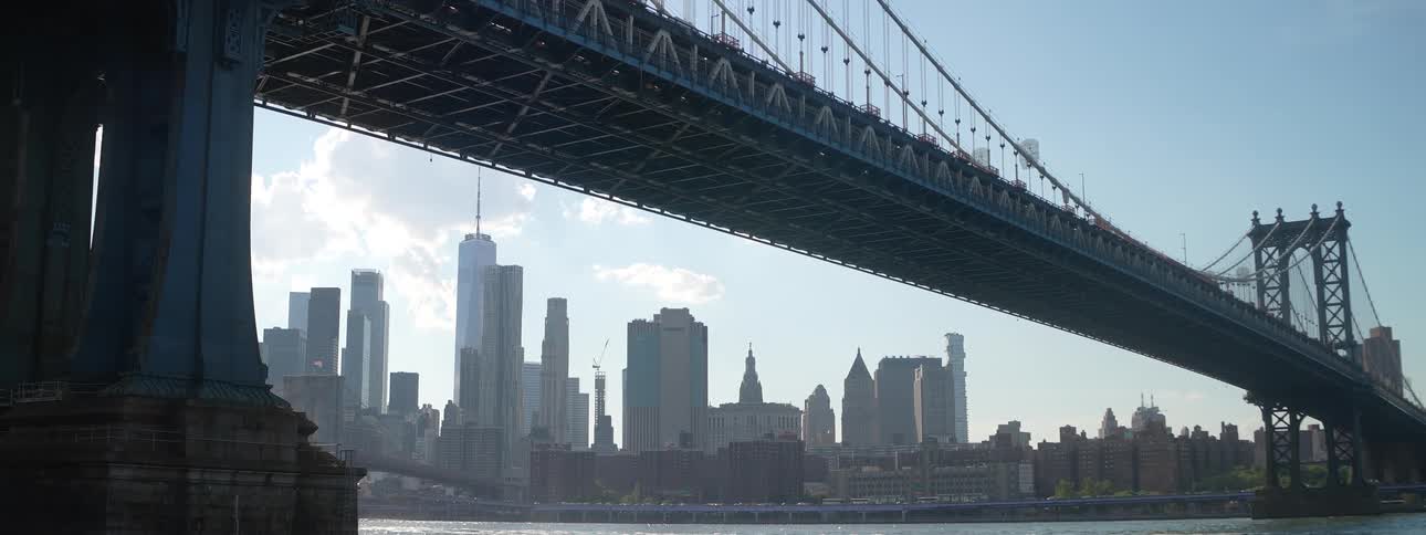 Metal bridge spans the river with skyscrapers in the background under a clear sky