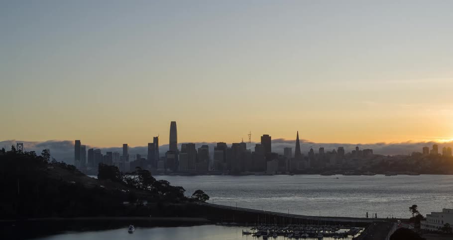 Aerial of a flowing water body before a metropolitan landscape at sunset