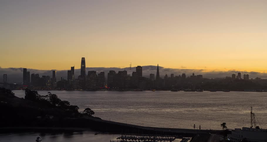 The sun is rising over the mountains near a city on a river