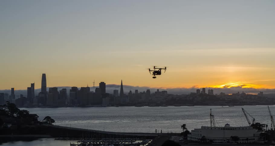 Drone flies over the bay at dawn with the city and rising sun in the background