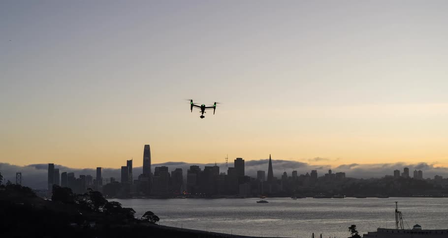 Drone flies over the bay in front of the city skyline at sunset