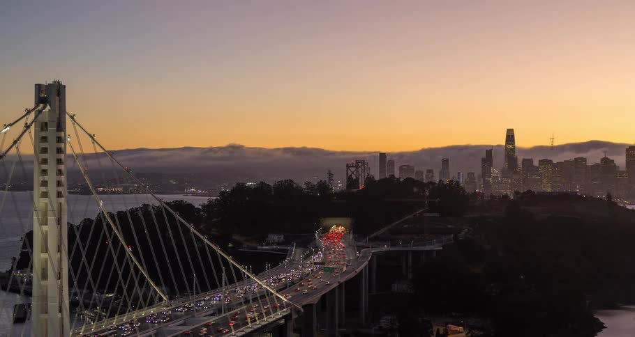 Traffic on a hanging bridge leading to an island with a metropolitan area on the background during dusk or dawn