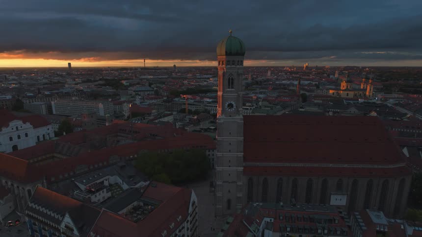 Two identical towers atop a building in the middle of a city with gray clouds in the sky