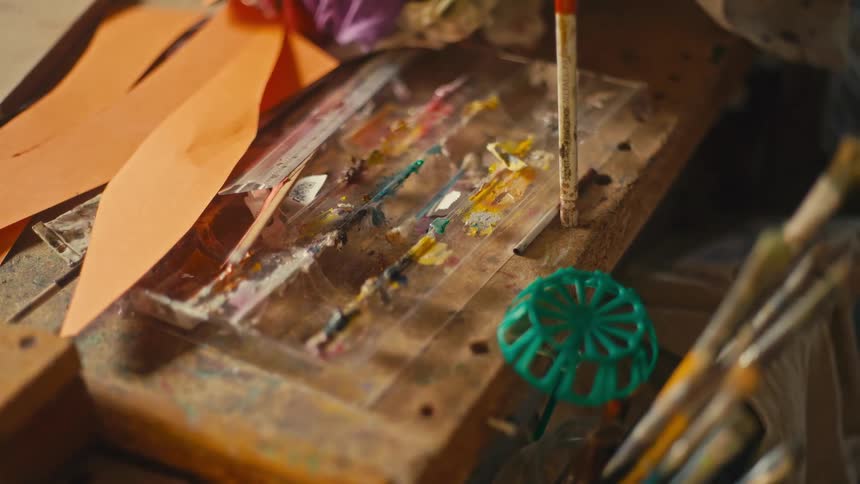 Paintbrushes and a dried paint stained palette sit on a bench in a workshop