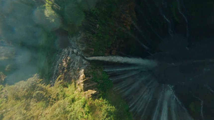 Waterfall plunges between cliffs covered in dense vegetation