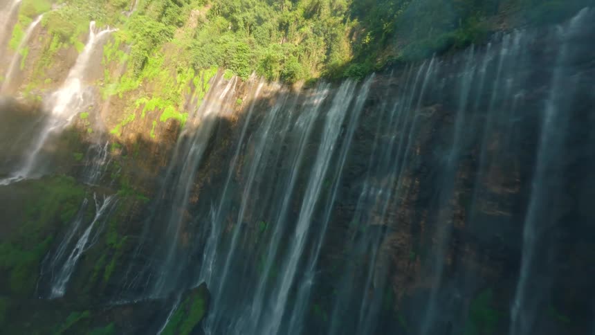 Waterfall flows down a mosscovered cliff lit by sunlight