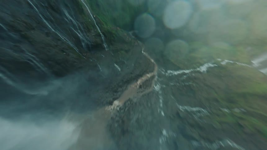 First person perspective from a drone flying down along side a waterfall