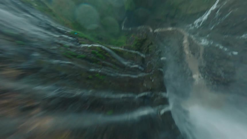 A massive sundrenched waterfall and the densely vegetated mosscovered cliffs of a deep canyon and a river flowing through the dark winding gorge below